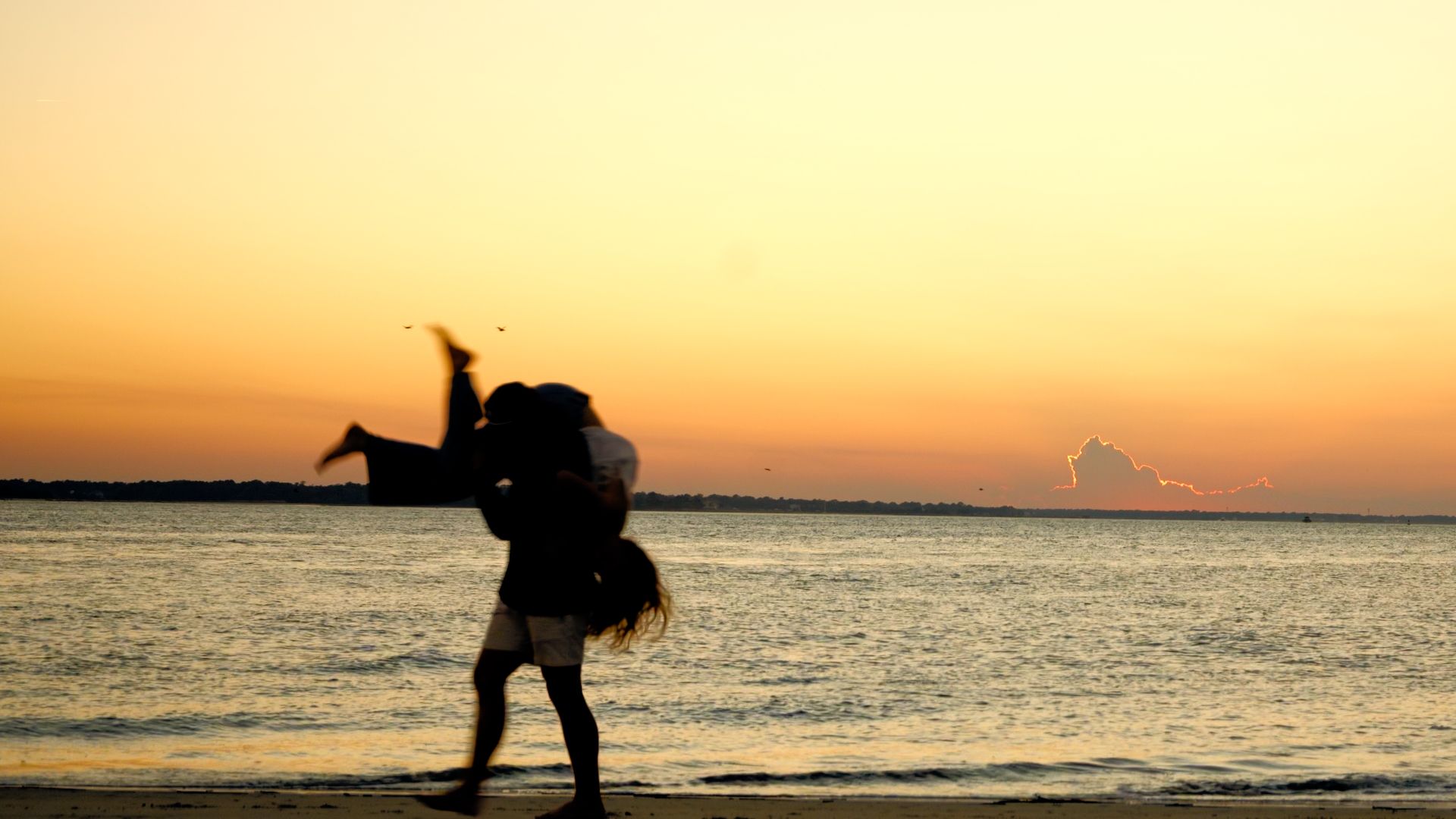 A couple silhouetted beside the water at sunset