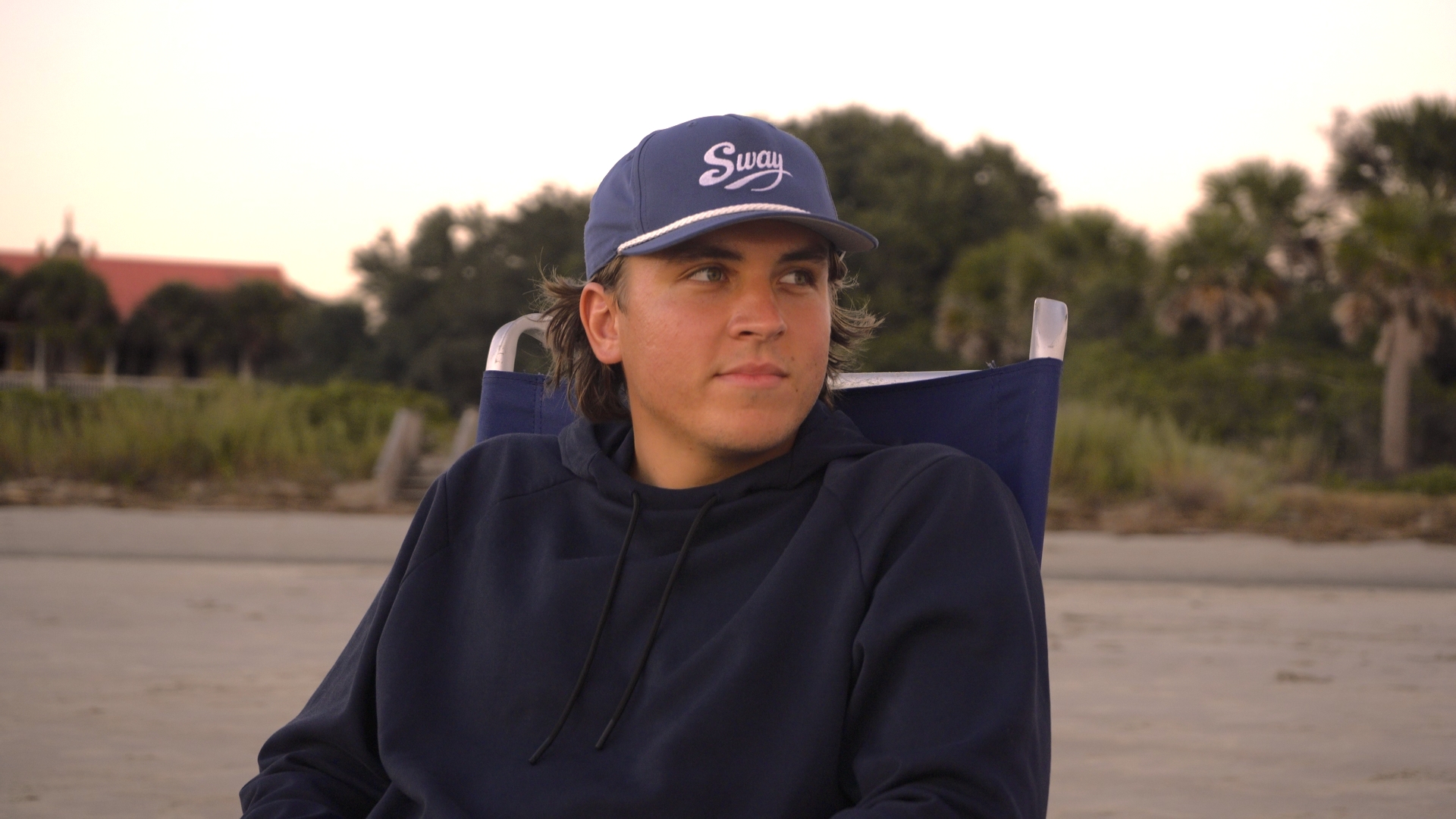 A person wearing a Sway cap seated near the coast